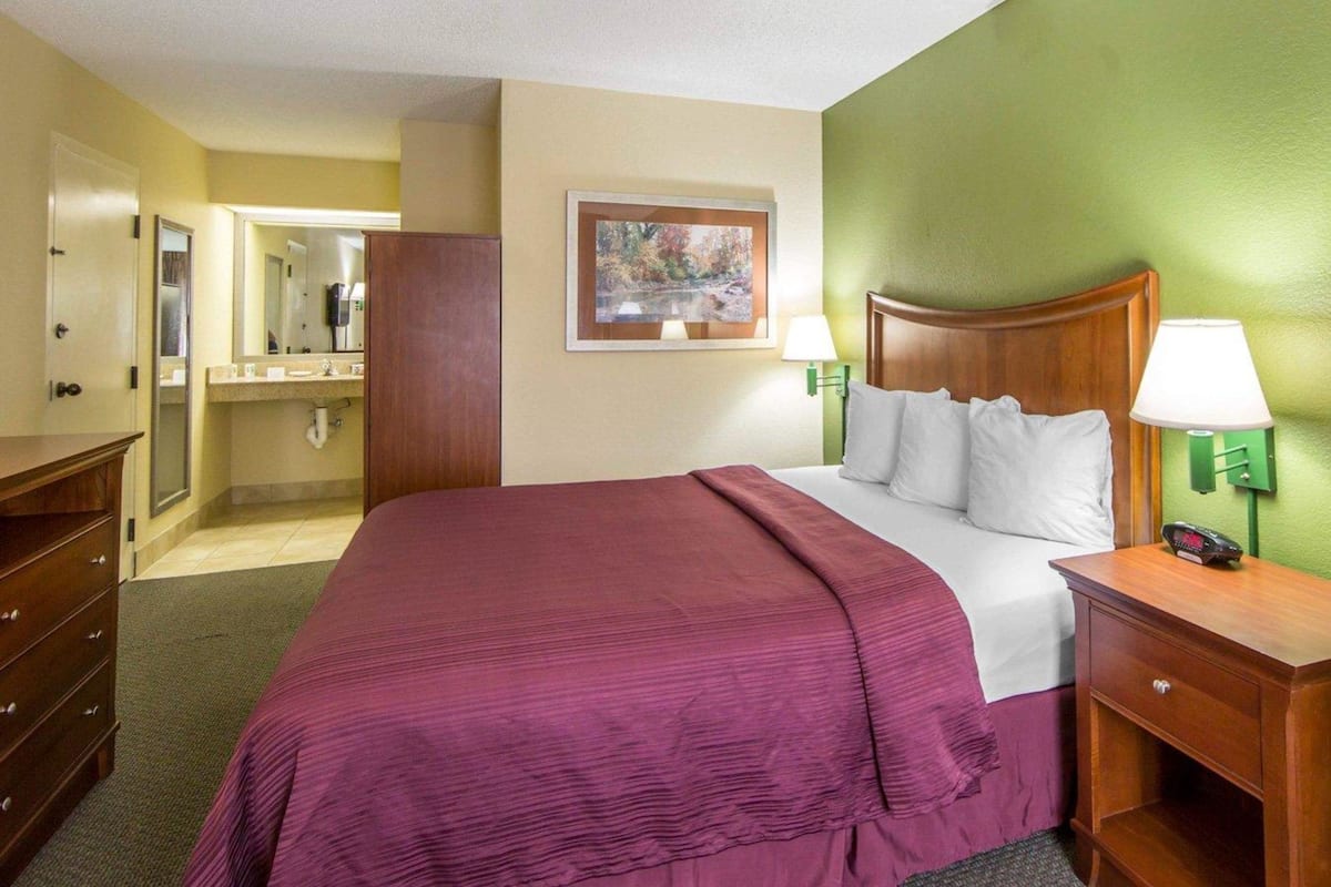 A hotel room with a bed, a dresser, a mirror, and a painting on the wall.