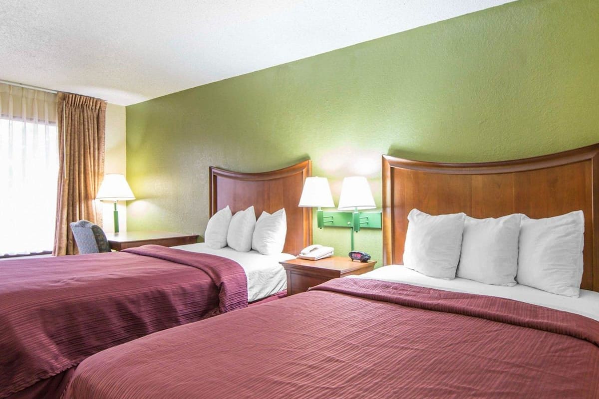 A hotel room with two beds, green walls, and a window with curtains.