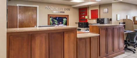 A hotel reception desk with a wooden counter, a fish tank, and a sign reading "Quality Inn By Choice Hotels".