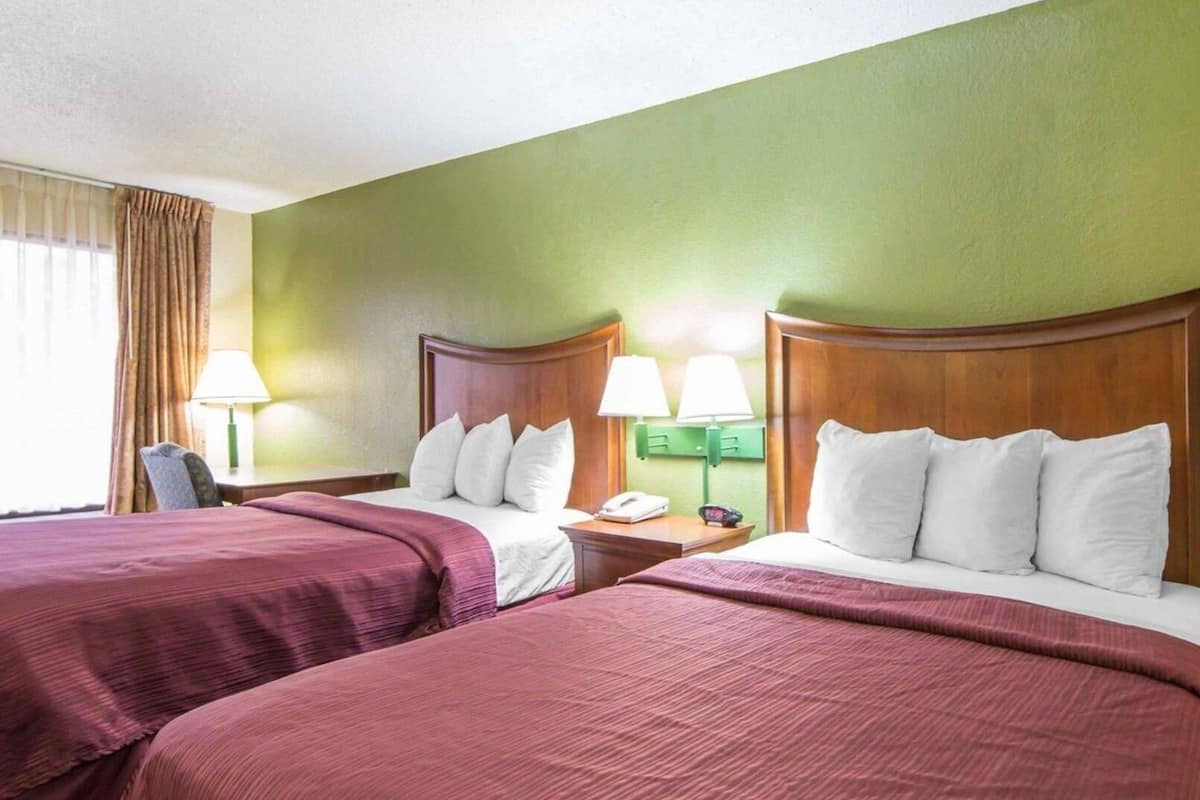 A hotel room with two beds, green walls, and a window with curtains.