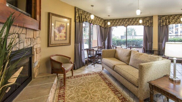 Una sala de estar con chimenea, un sofá, una mesa de comedor con sillas y ventanas grandes con cortinas.