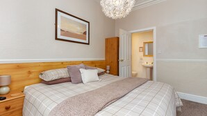 A bedroom with a bed, wooden headboard, a framed picture on the wall, a hanging light fixture, and a door leading to a bathroom. - The Chorlton (Blackpool)