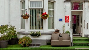A white building with a bay window, a front door, and a small porch with a wicker sofa. - The Chorlton (Blackpool)