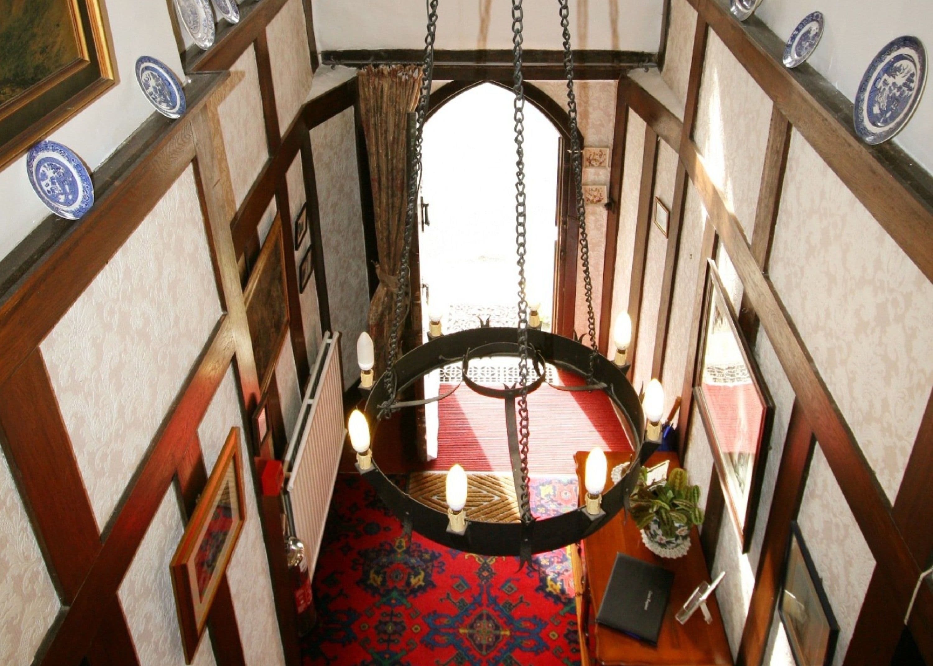 A narrow hallway with a red carpet, wooden paneling, and a hanging light fixture.