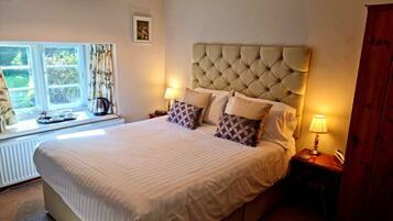 A well-lit bedroom with a large bed, a window with curtains, a bedside table with a lamp, and a radiator.