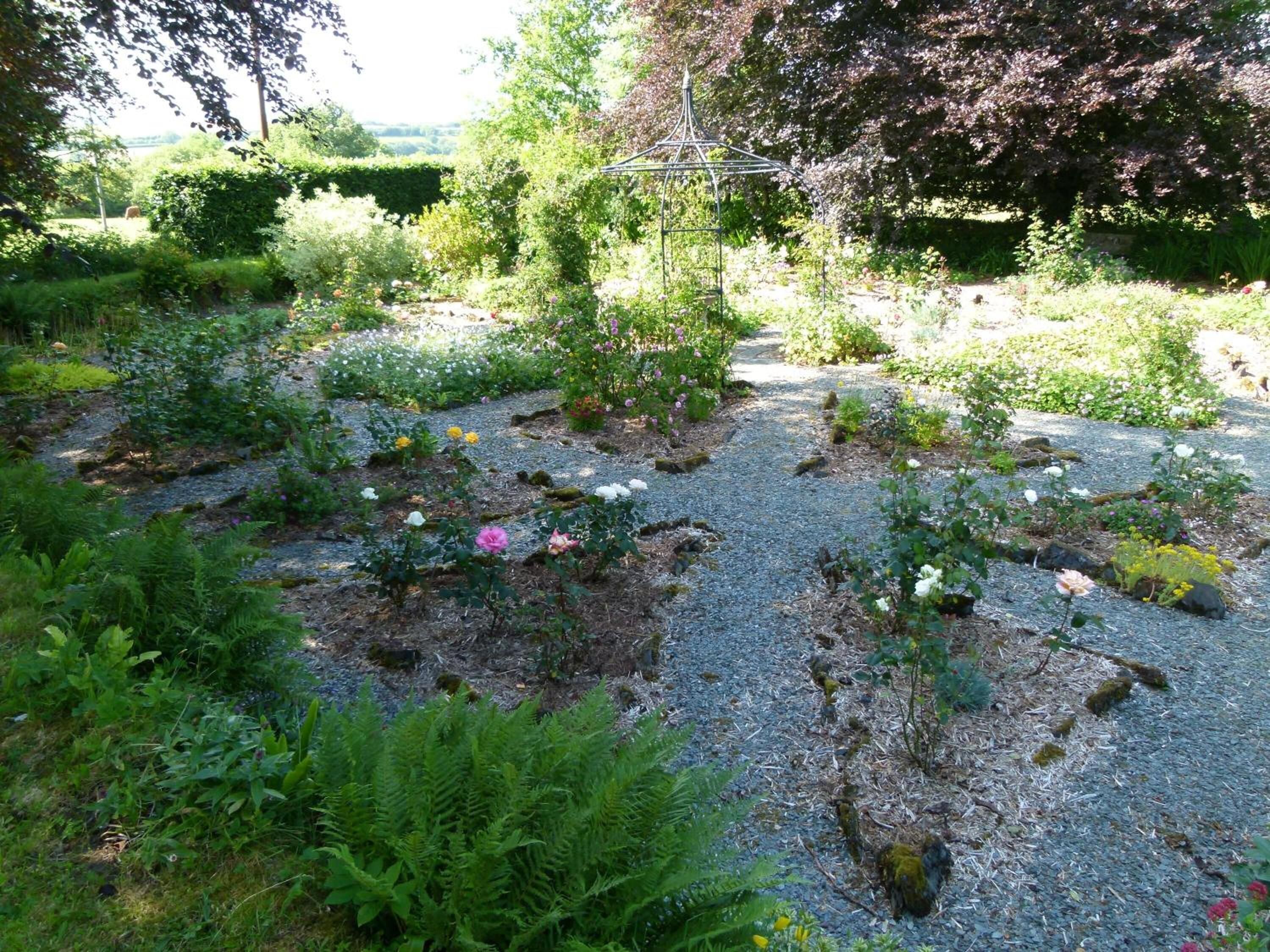 A garden with a variety of plants and flowers, a metal gazebo, and a gravel path.
