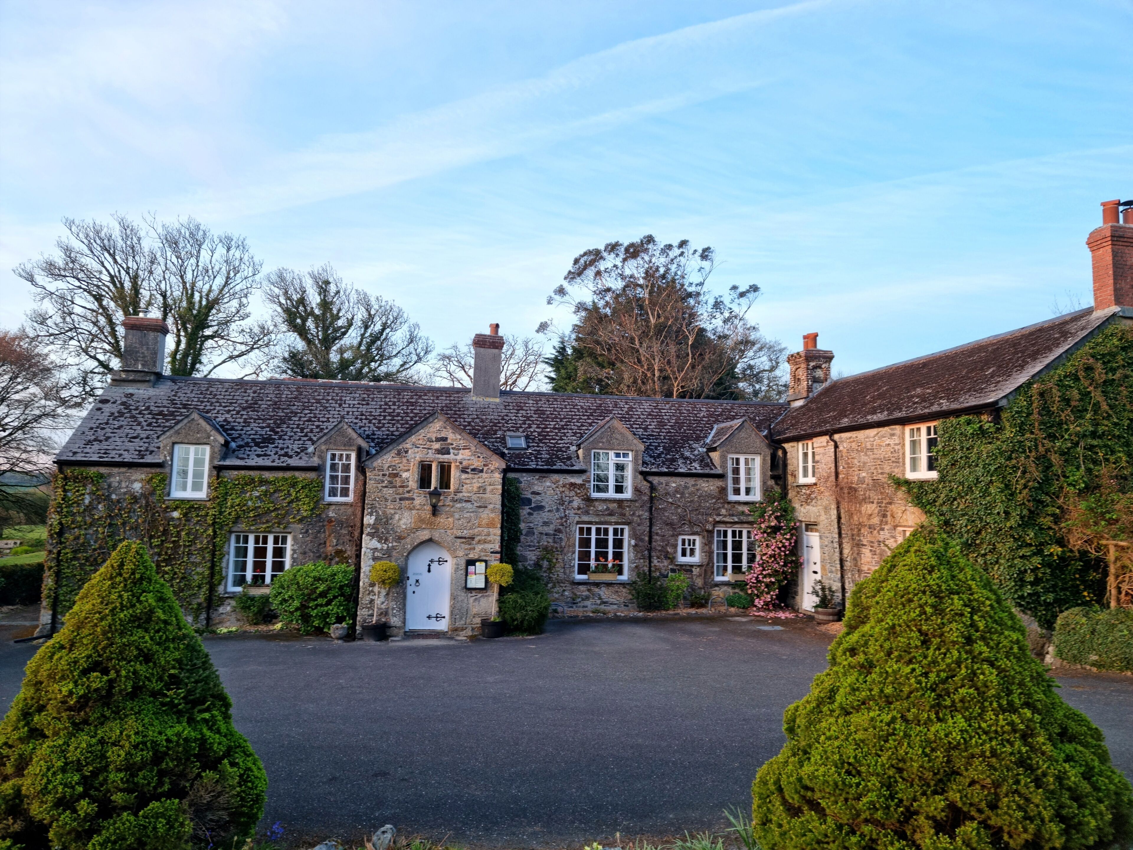 A stone building with a central entrance, multiple windows, and a paved driveway.