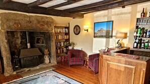 A cozy living room with a stone fireplace, a bookshelf, plaid chairs, and a bar area with bottles. - Collaven Manor Hotel (Okehampton)