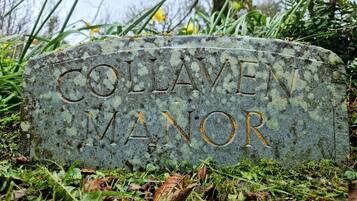 A stone headstone with the inscription "Collaven Manor" surrounded by greenery.
