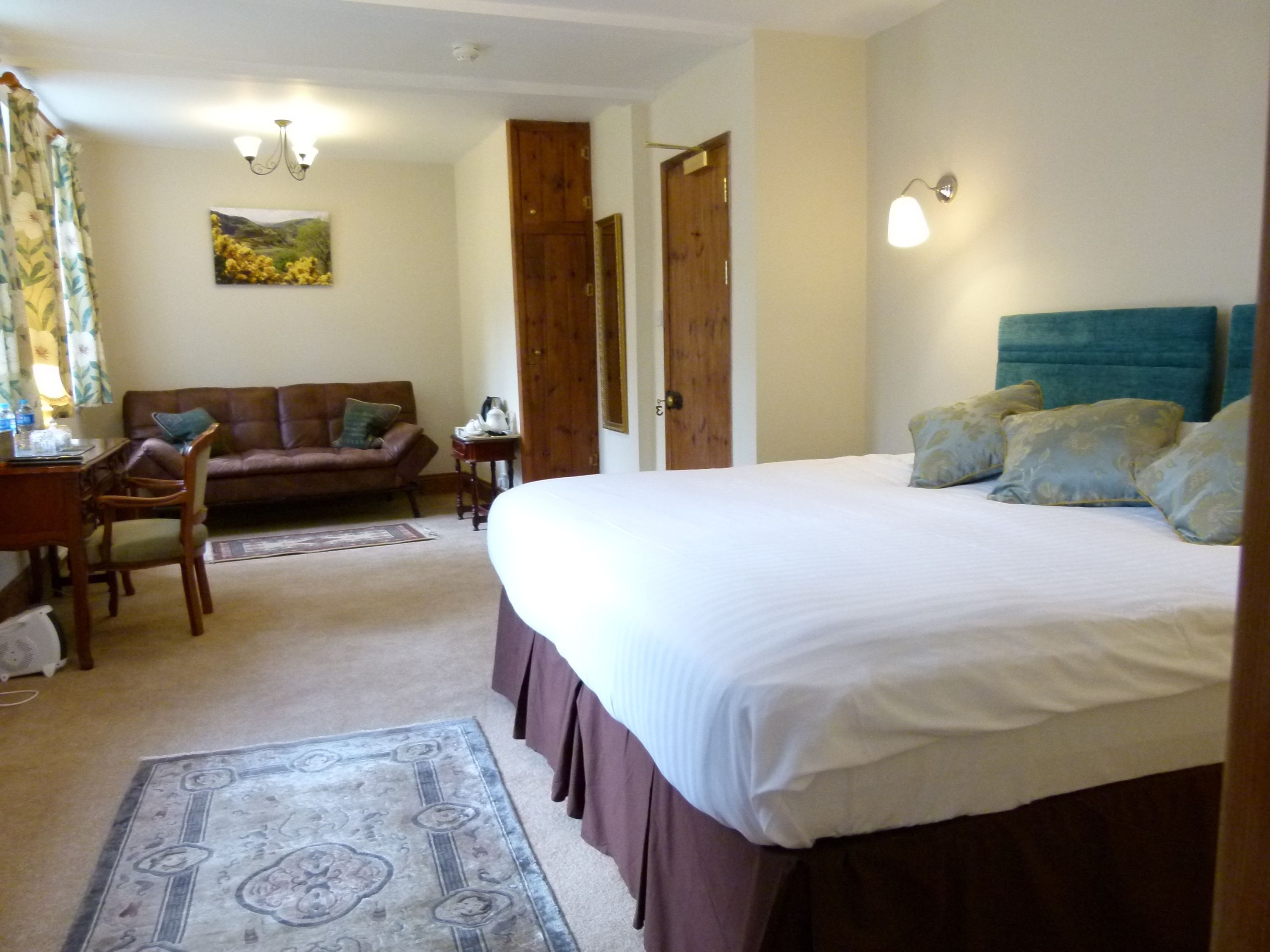 A bedroom with a large bed, a wooden wardrobe, a sitting area with a sofa and chairs, and a small table.
