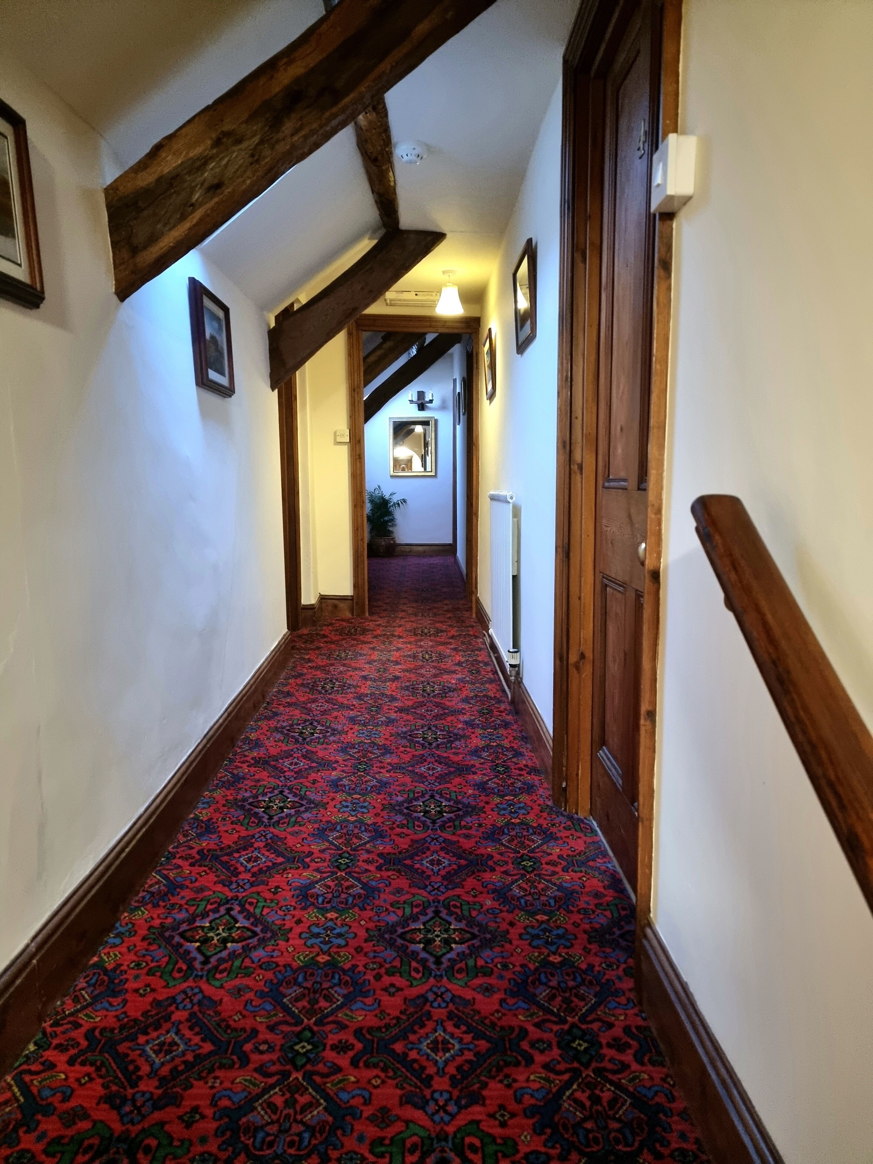 A hallway with a patterned carpet, wooden beams, and a door on the right.