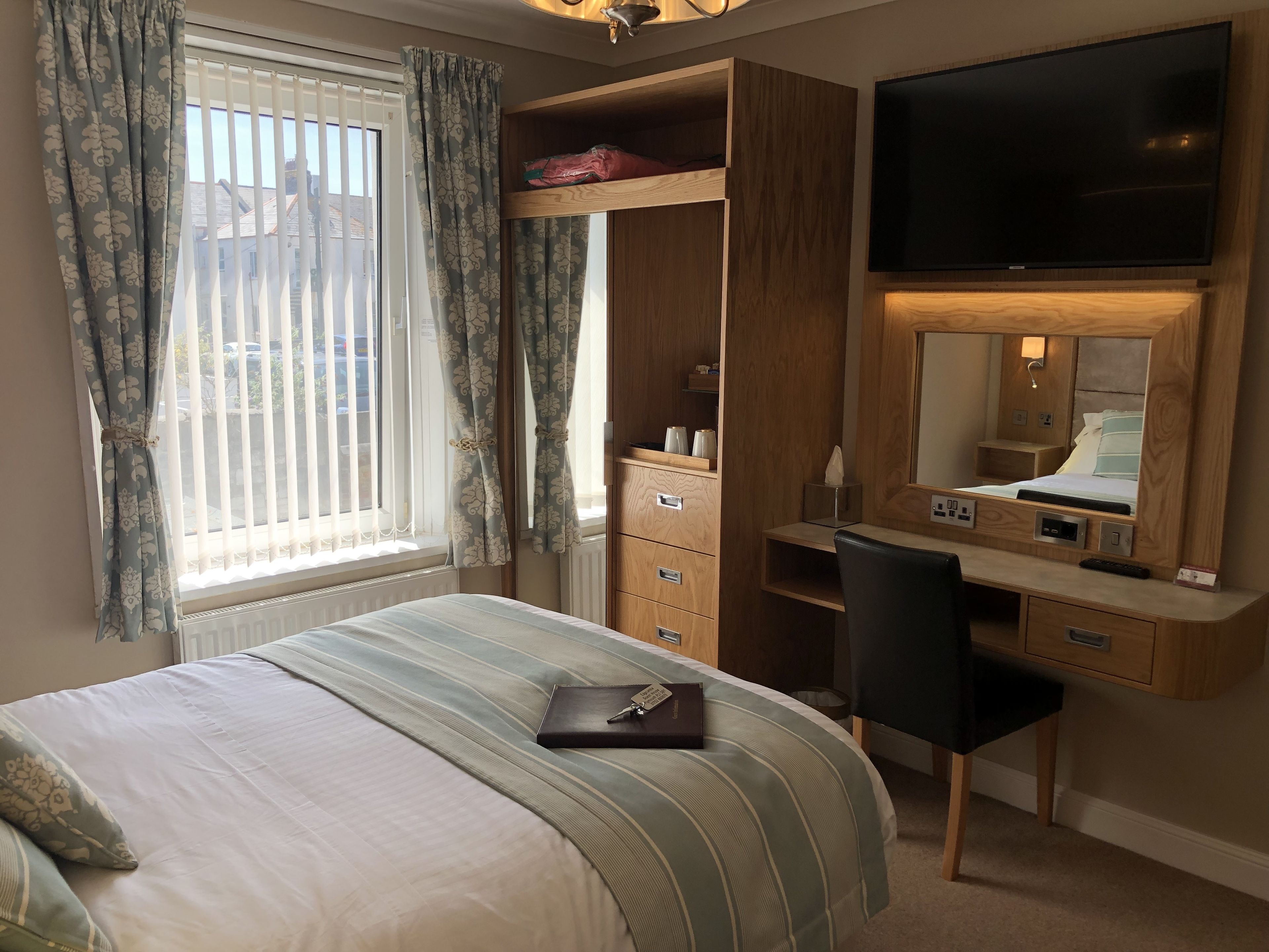 A bedroom with a bed, a desk, a chair, a TV, and a wardrobe.