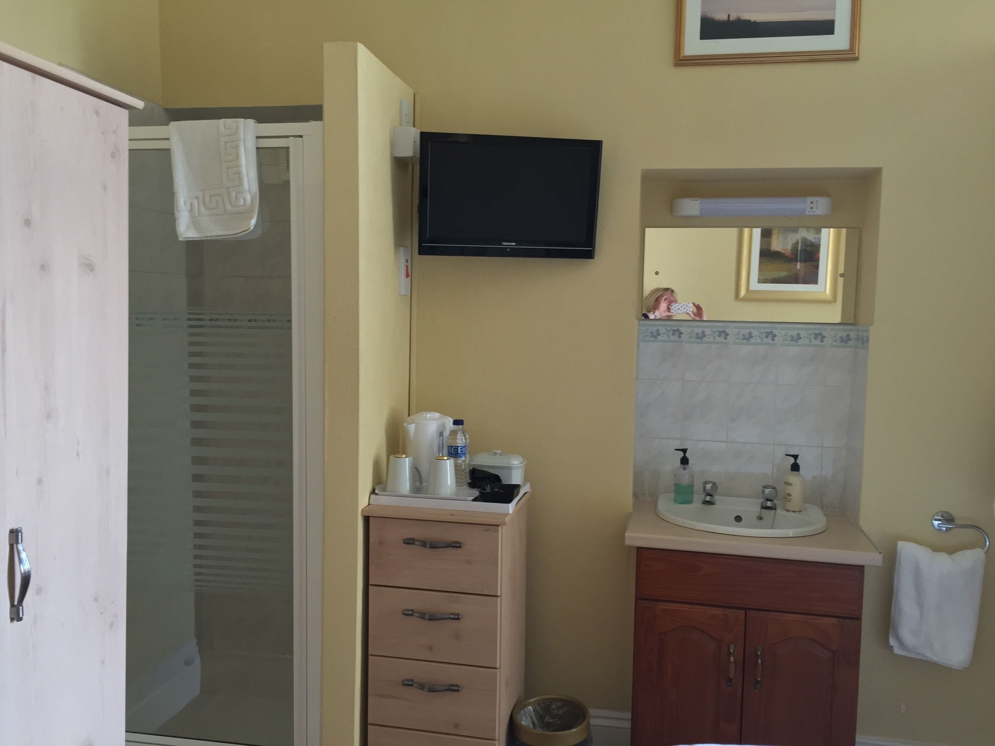 Een badkamer met een douche, wastafel, spiegel en een aan de muur bevestigde televisie.
