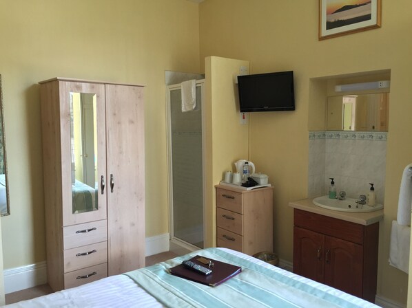 A bedroom with a bed, a wardrobe, a bathroom with a sink, and a TV mounted on the wall.