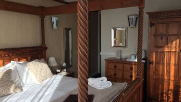 A four-poster bed with a wooden headboard, a bedside table with a lamp, a mirror, and a wooden dresser with a mirror.
