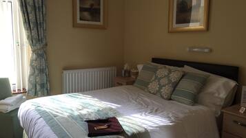 A neatly made bed with a striped bedspread, a bedside table with a lamp, and two framed pictures on the wall.