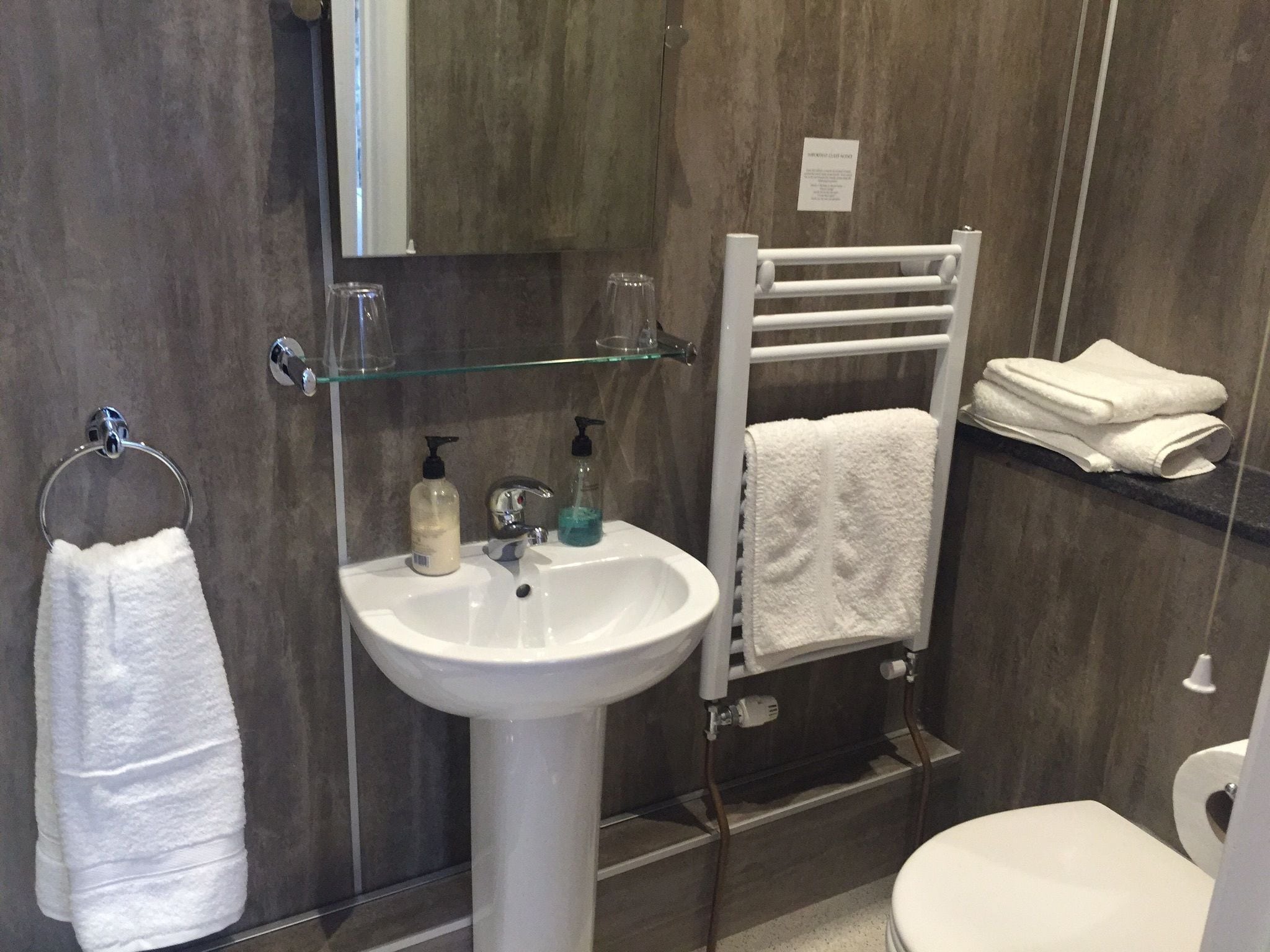 A bathroom with a white sink, a glass shelf, a towel rack, and a toilet.