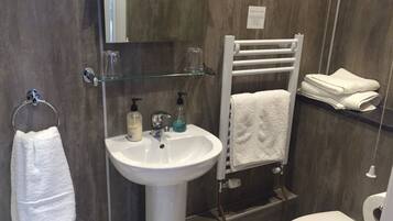 A bathroom with a white sink, a glass shelf, a towel rack, and a toilet.