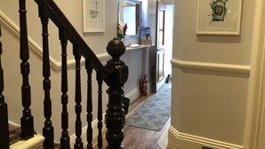 A hallway with a wooden staircase, framed artwork on the walls, and a fire extinguisher near the door. - Edgcumbe Guest House (Plymouth)