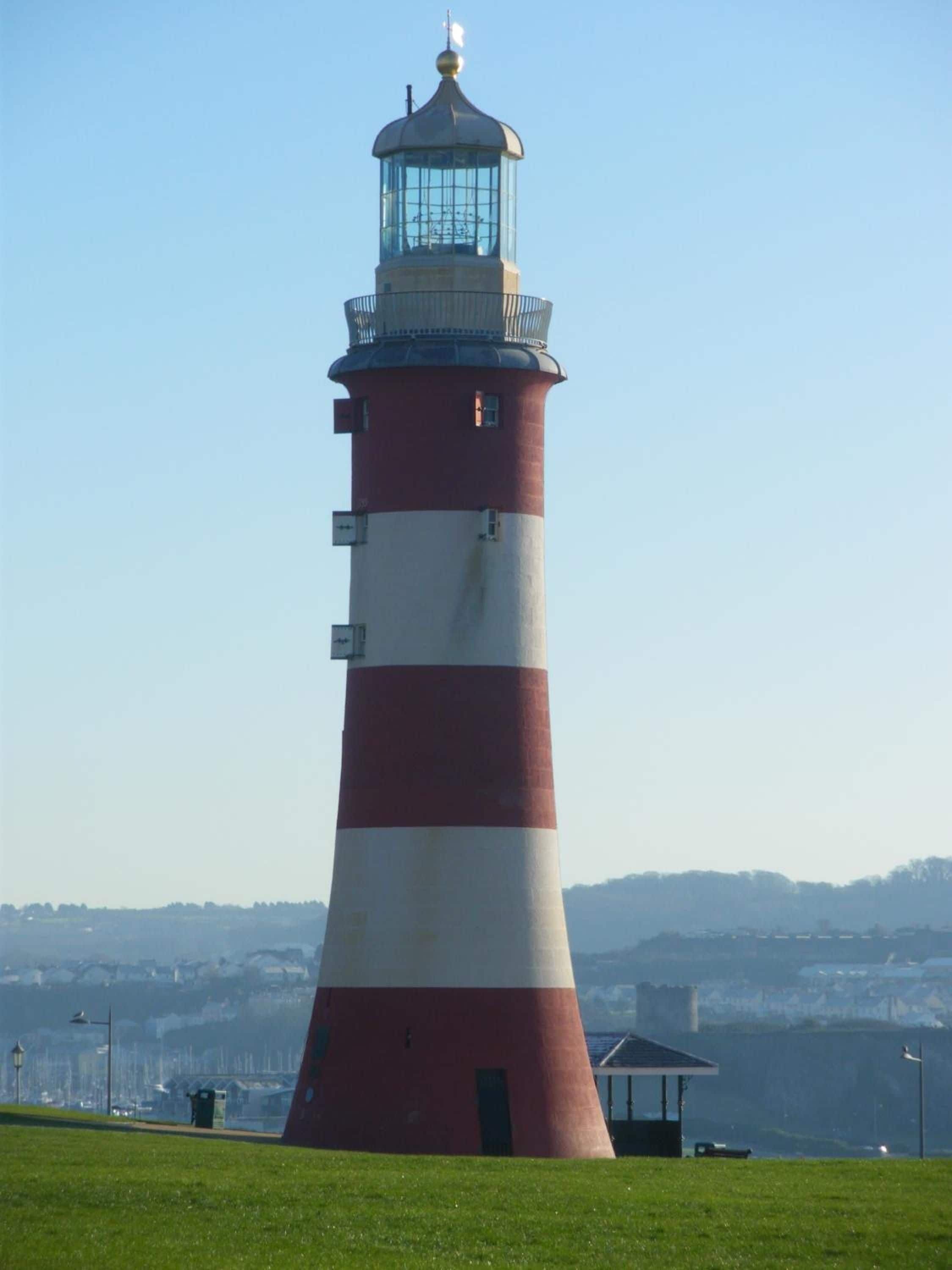 A tall lighthouse with a red and white striped tower, a glass lantern room, and a small adjacent structure.