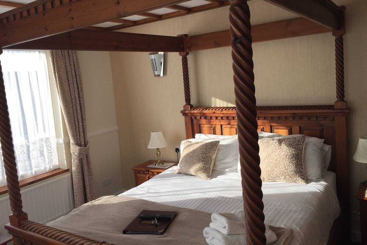 Ein Bett mit Baldachin, einem Holzkopfstück, weißer Bettwäsche und einer Fernbedienung auf dem Bett.
