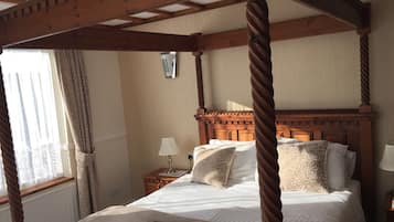 Ein Bett mit Baldachin, einem Holzkopfstück, weißer Bettwäsche und einer Fernbedienung auf dem Bett.