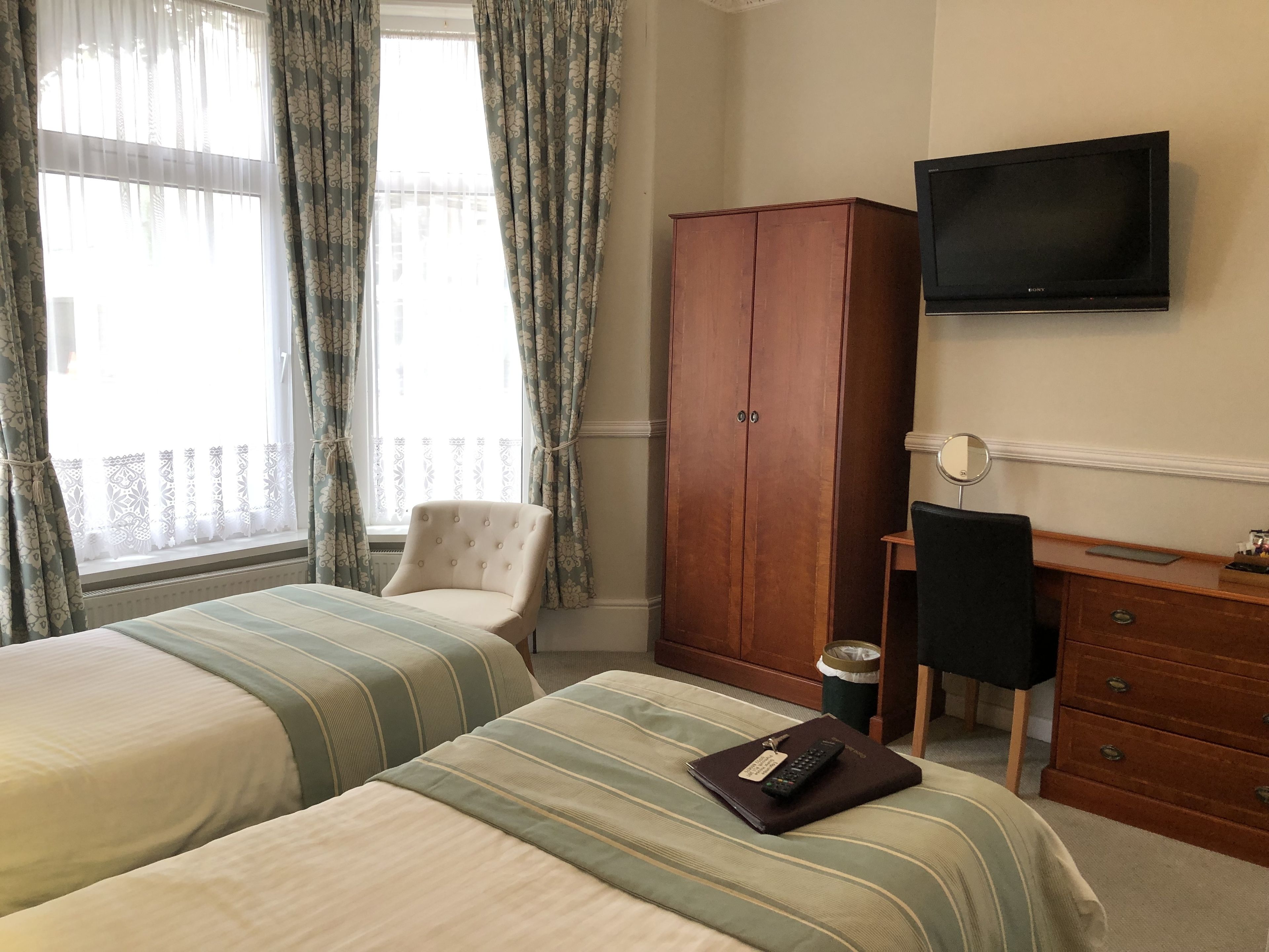Ett hotellrum med två sängar, en garderob i trä, en TV och ett litet skrivbord med en stol.