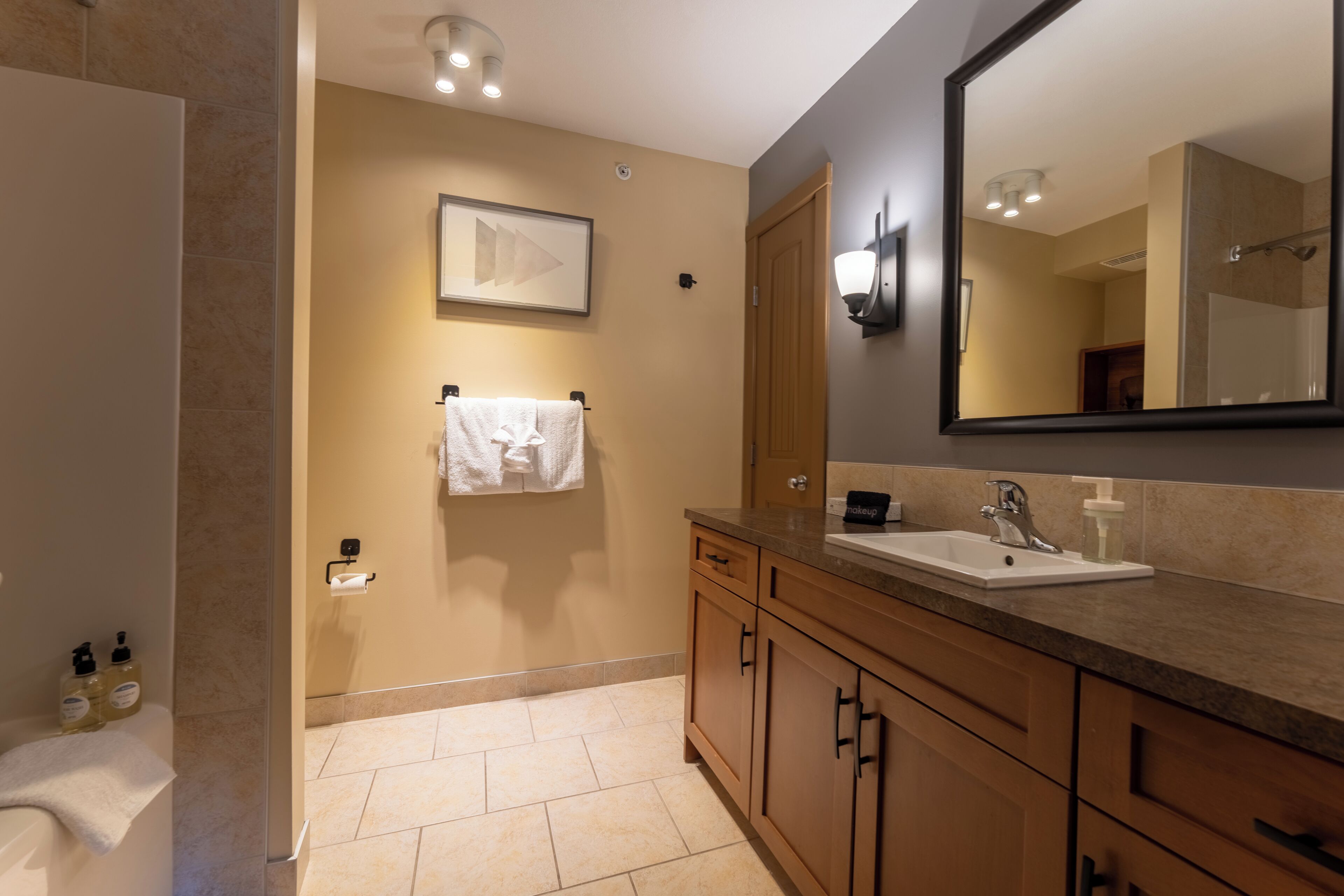 A modern bathroom with a large mirror, wooden cabinets, a sink, and a shower area.