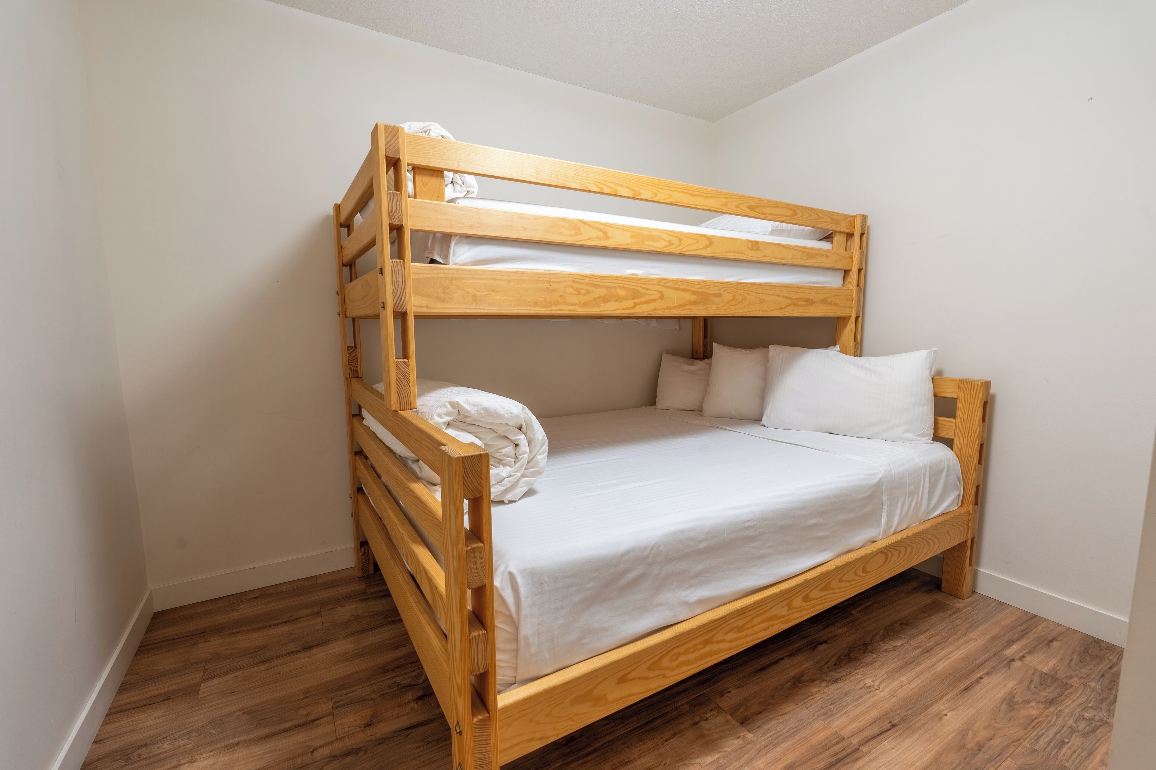A bunk bed with white bedding in a room with wooden flooring and white walls.