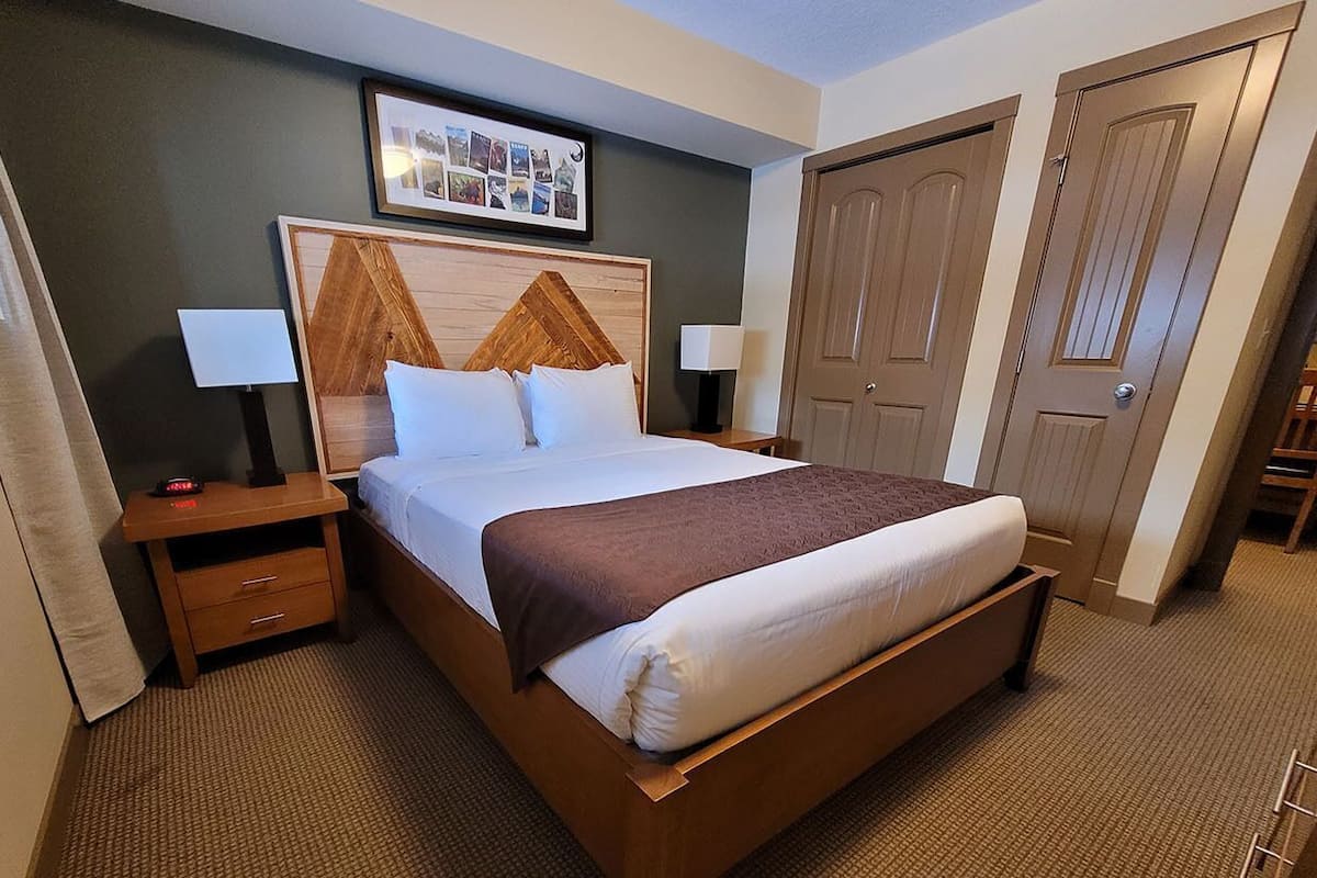 Habitación de hotel con cama, mesitas de noche, cabecera, una fotografía enmarcada en la pared y una puerta.