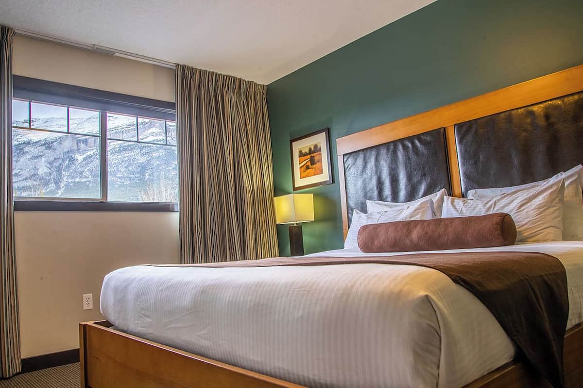 Una habitación de hotel con una cama, una ventana con cortinas, una lámpara y un cuadro en la pared.