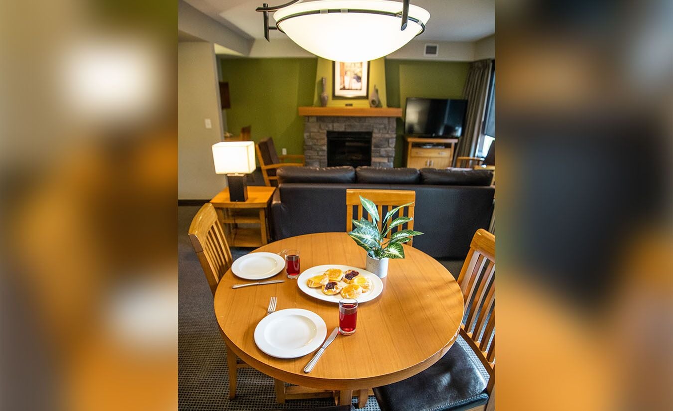 A dining area with a round wooden table, two chairs, a potted plant, and a plate of food.