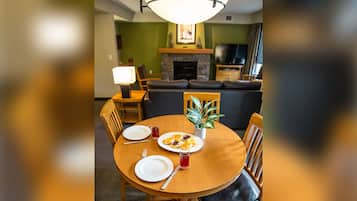 A dining area with a round wooden table, two chairs, a potted plant, and a plate of food.