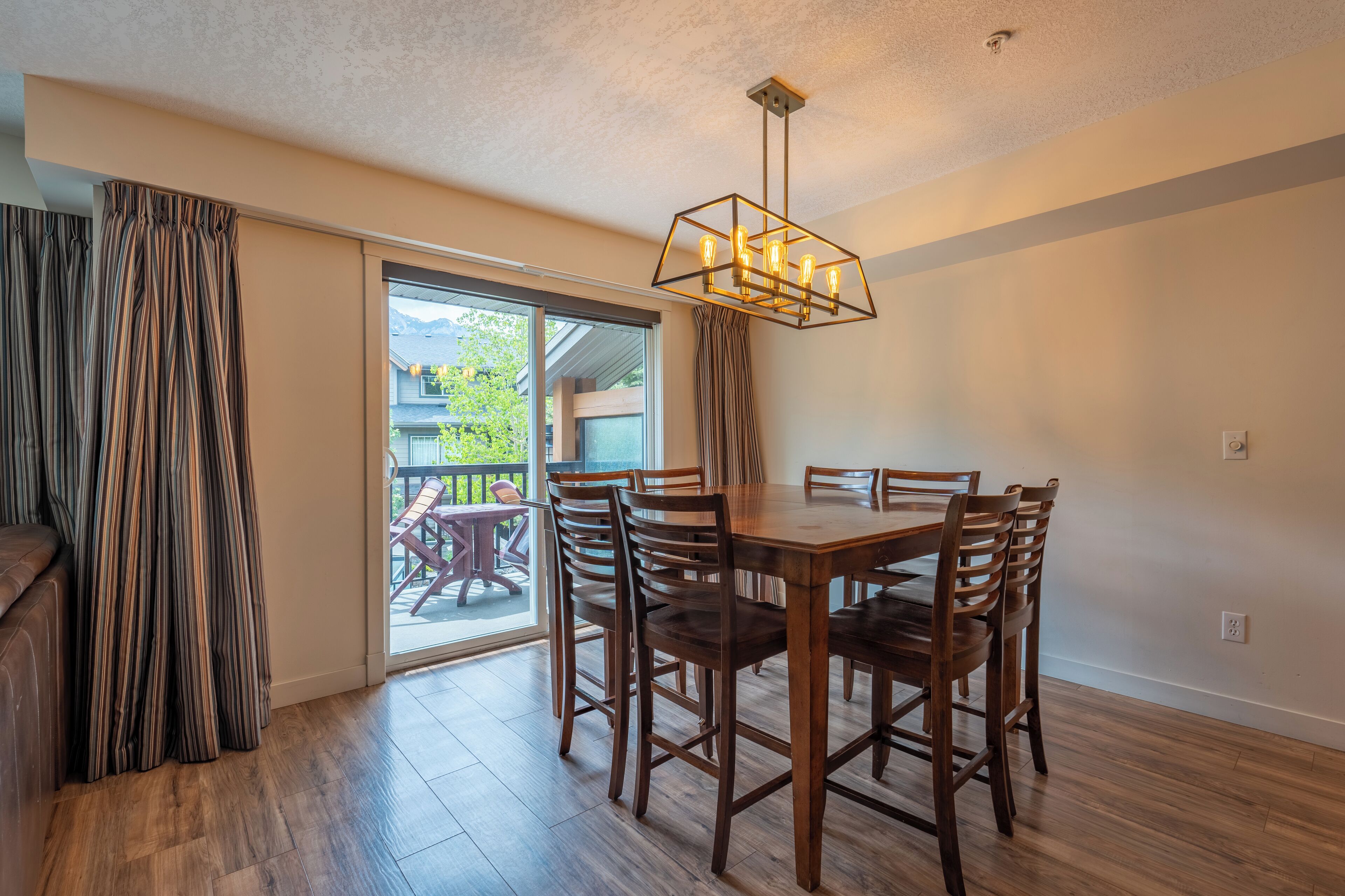 A dining area with a wooden table and chairs, a chandelier, and a sliding glass door leading to an outdoor patio.