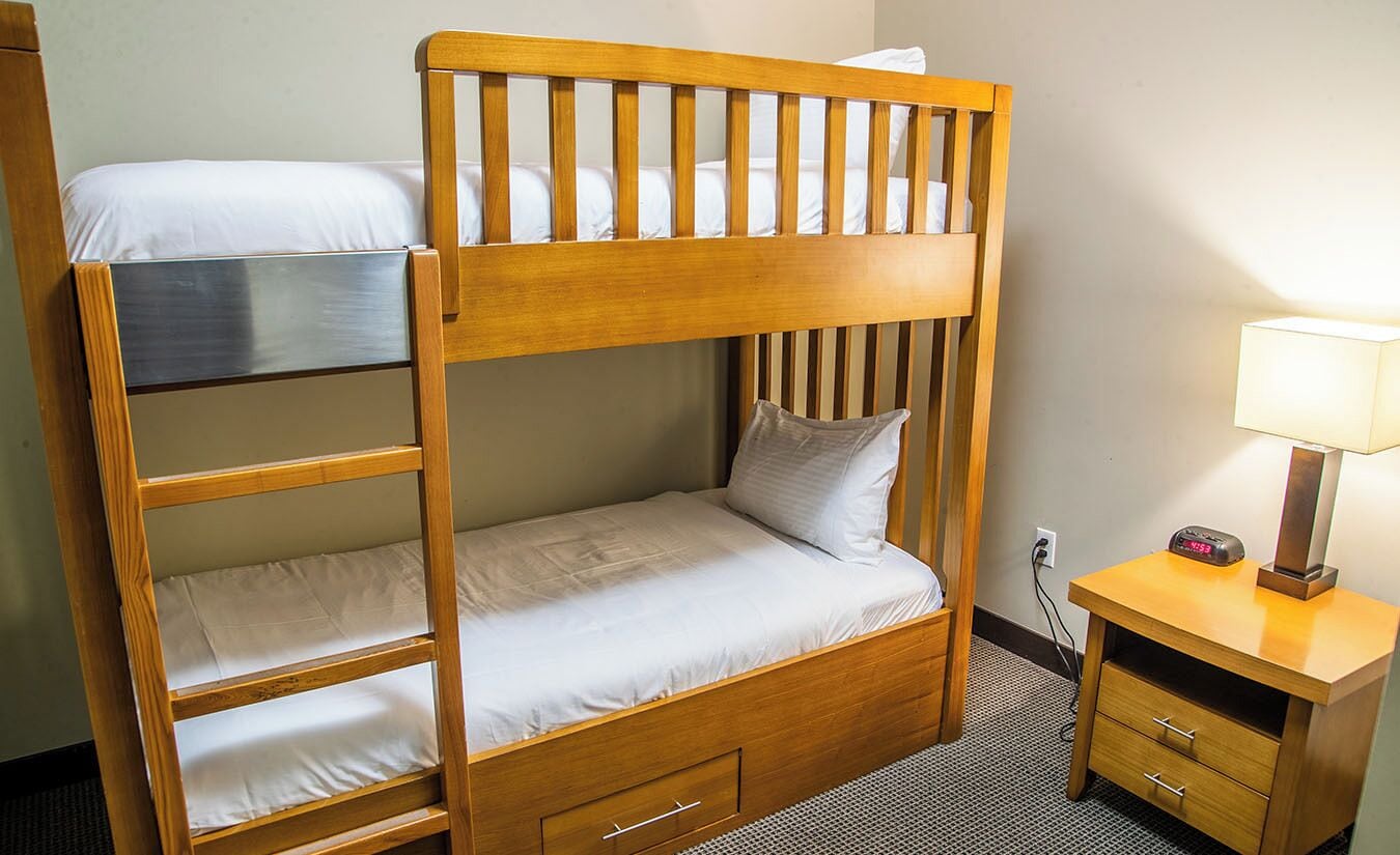 Una cama individual superpuesta con escritorio, lámpara, toma de corriente e interruptor de pared.