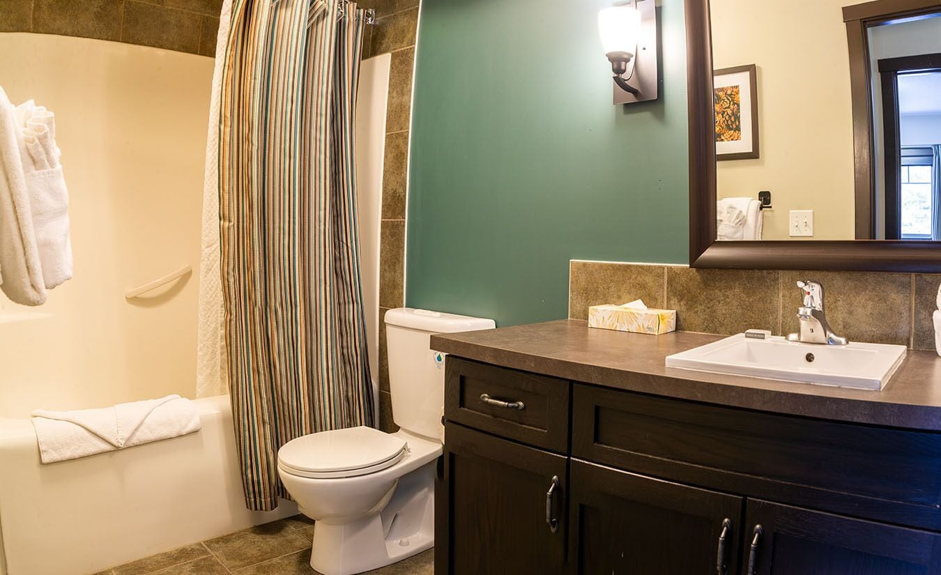 A bathroom with a white toilet, a shower curtain, a sink with a mirror, and a towel rack.