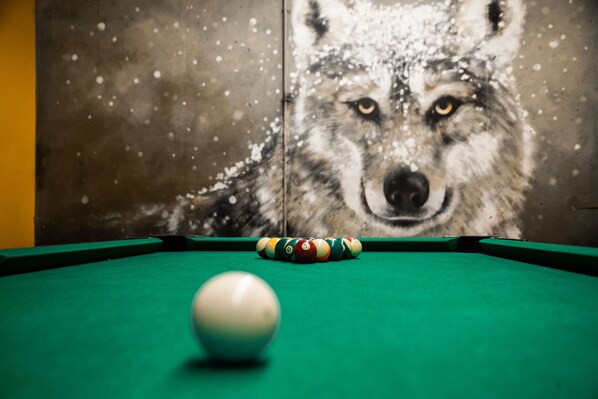 Une table de billard avec une boule blanche et des boules rayées, une fresque représentant un loup en arrière-plan et un tapis vert.