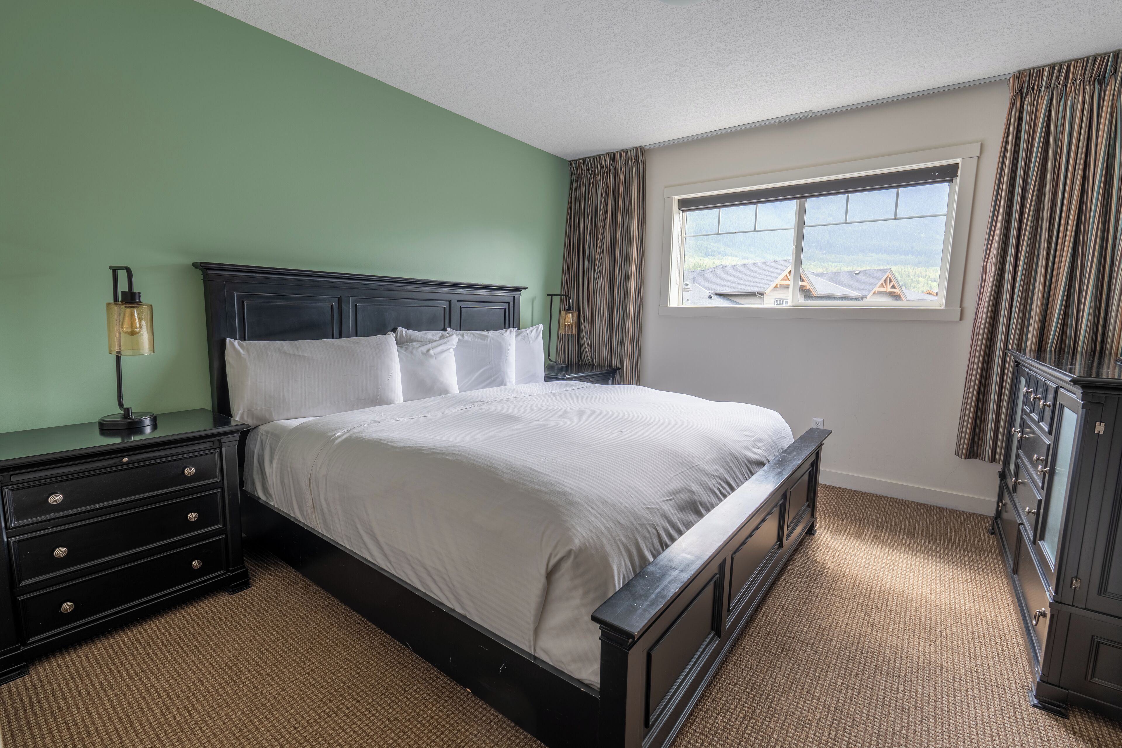 A neatly made bed in a room with green walls, a window with curtains, and a dresser.
