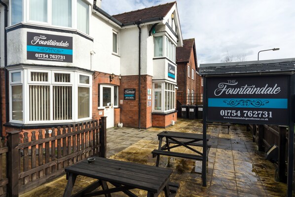 A building with a sign reading "The Fountaindale" and a contact number. There are picnic tables and a wooden fence in the foreground. - The Fountaindale (Skegness)
