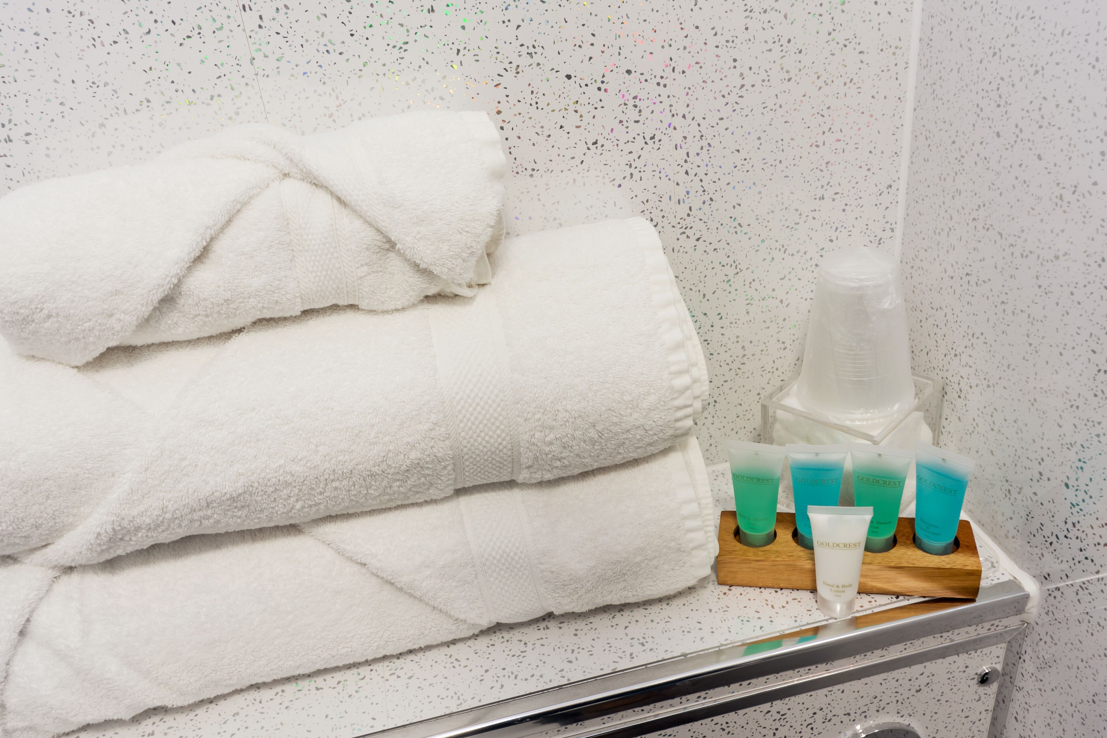 A bathroom with a stack of white towels and a tray of Gold Rest products.