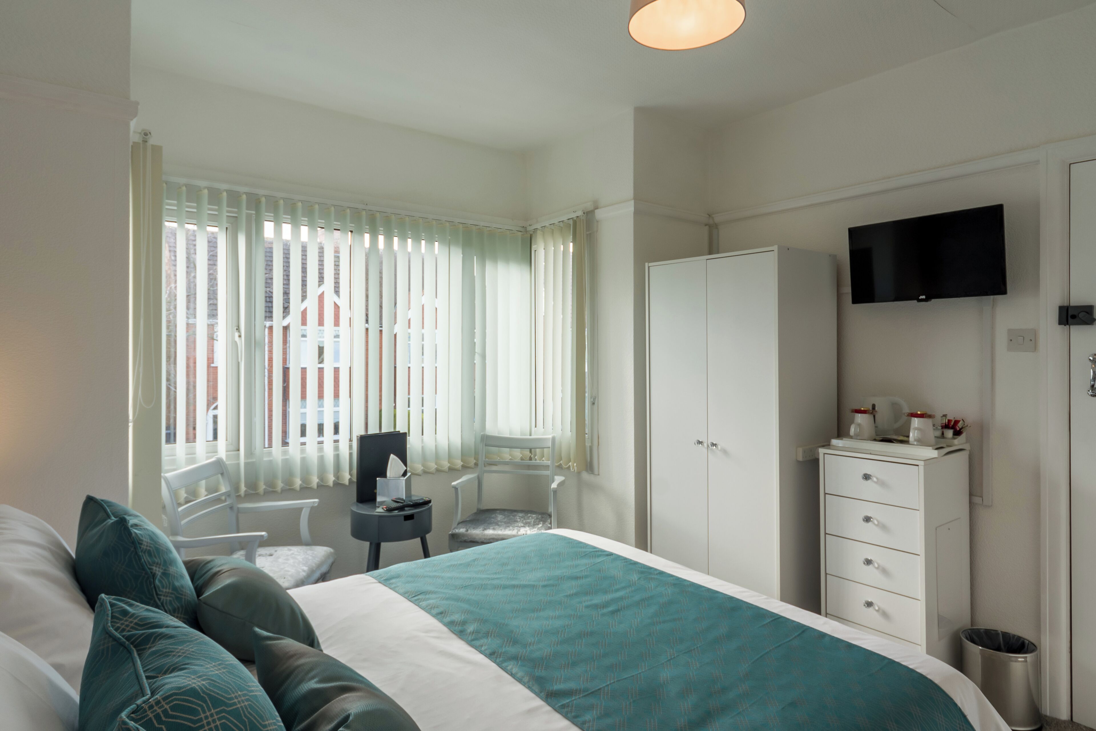 Une chambre d’hôtel équipée d’un lit, d’un bureau, d’une chaise, d’une armoire et d’un téléviseur fixé au mur.
