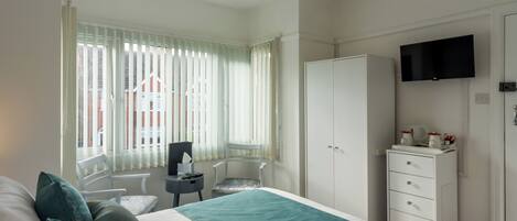 Une chambre d’hôtel équipée d’un lit, d’un bureau, d’une chaise, d’une armoire et d’un téléviseur fixé au mur.