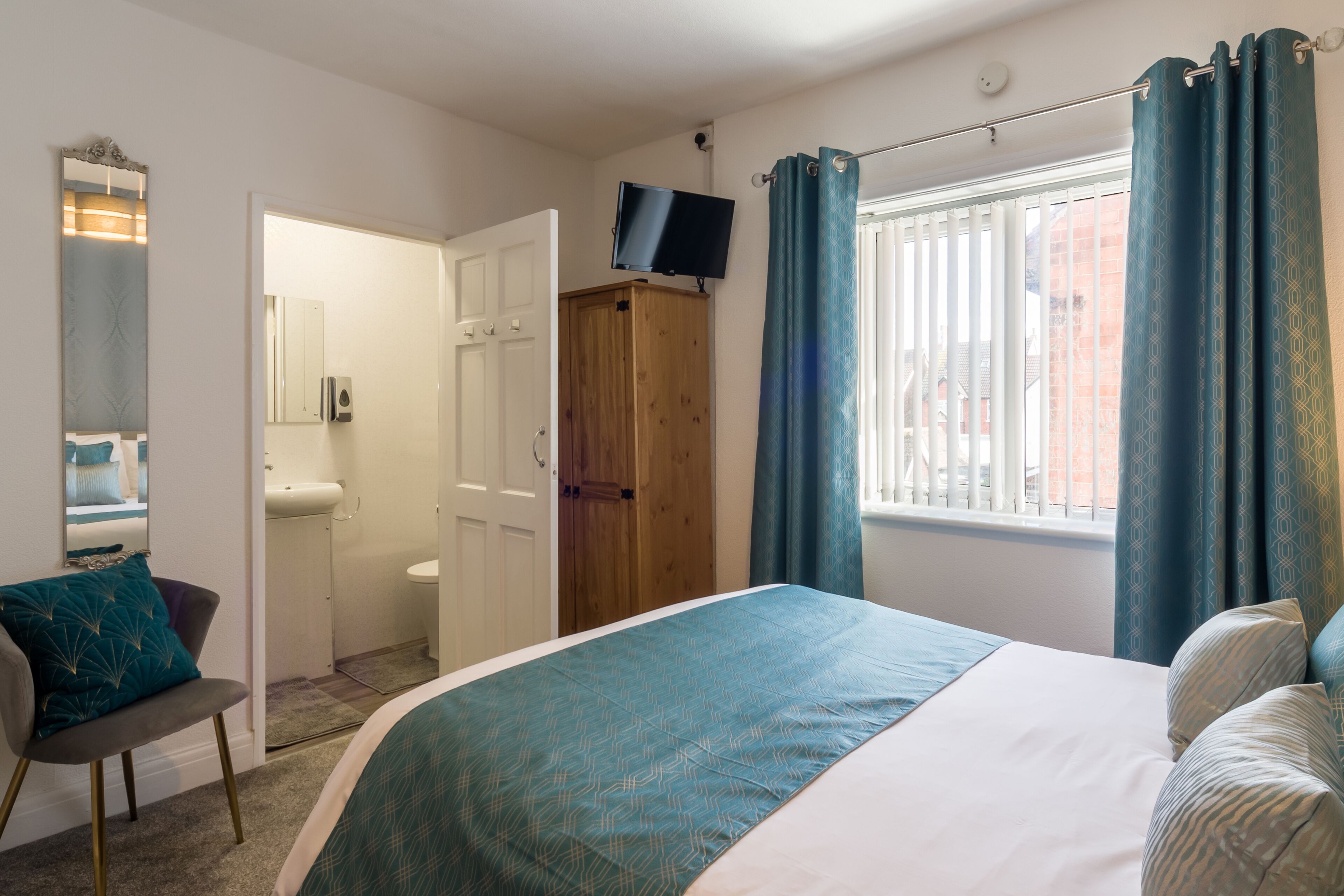 A bedroom with a bed, a TV, a wardrobe, a mirror, and a window with curtains.