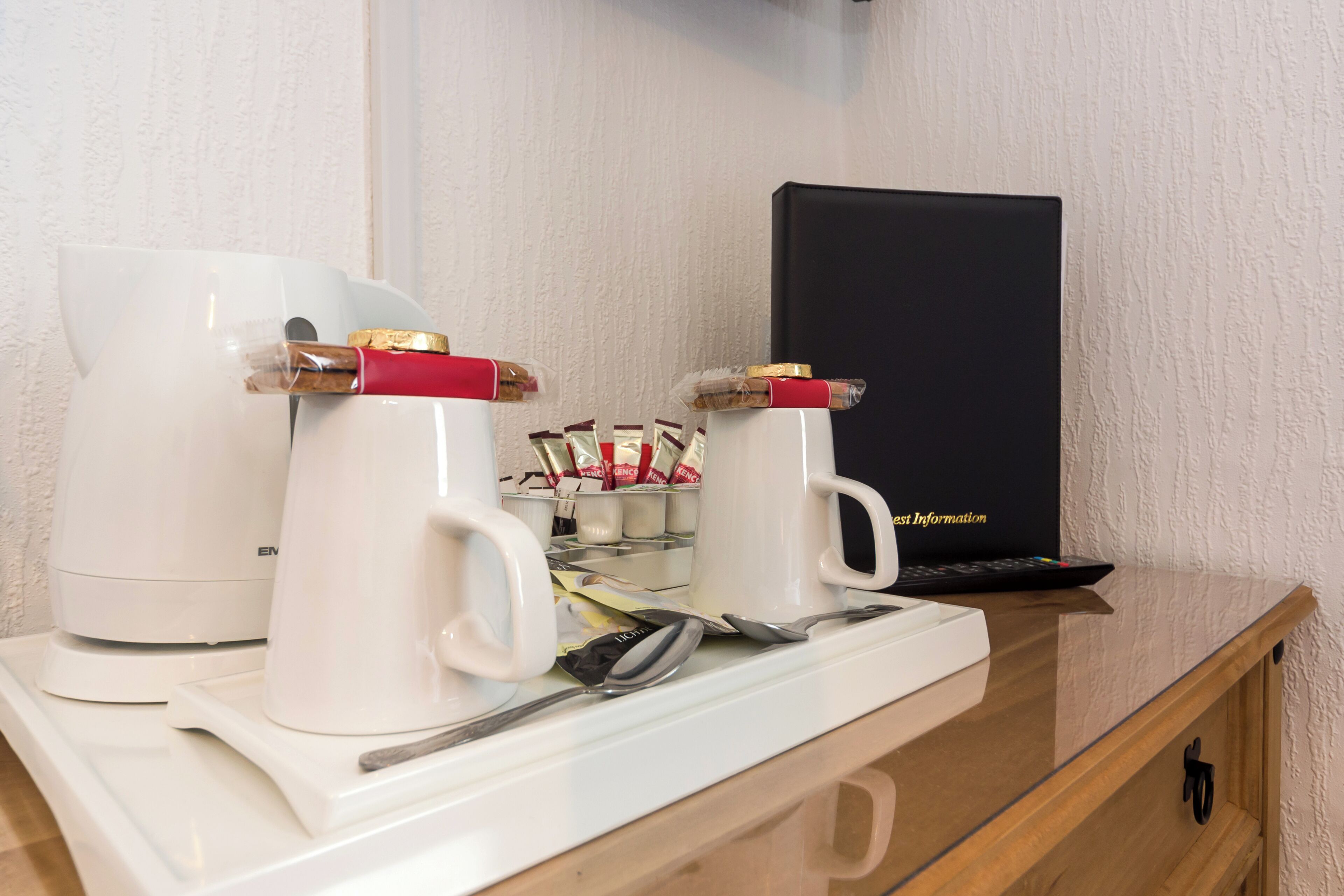 A kitchenette with a coffee maker, two mugs with coffee packets, a spoon, and a black box labeled "Best Information" on a countertop.