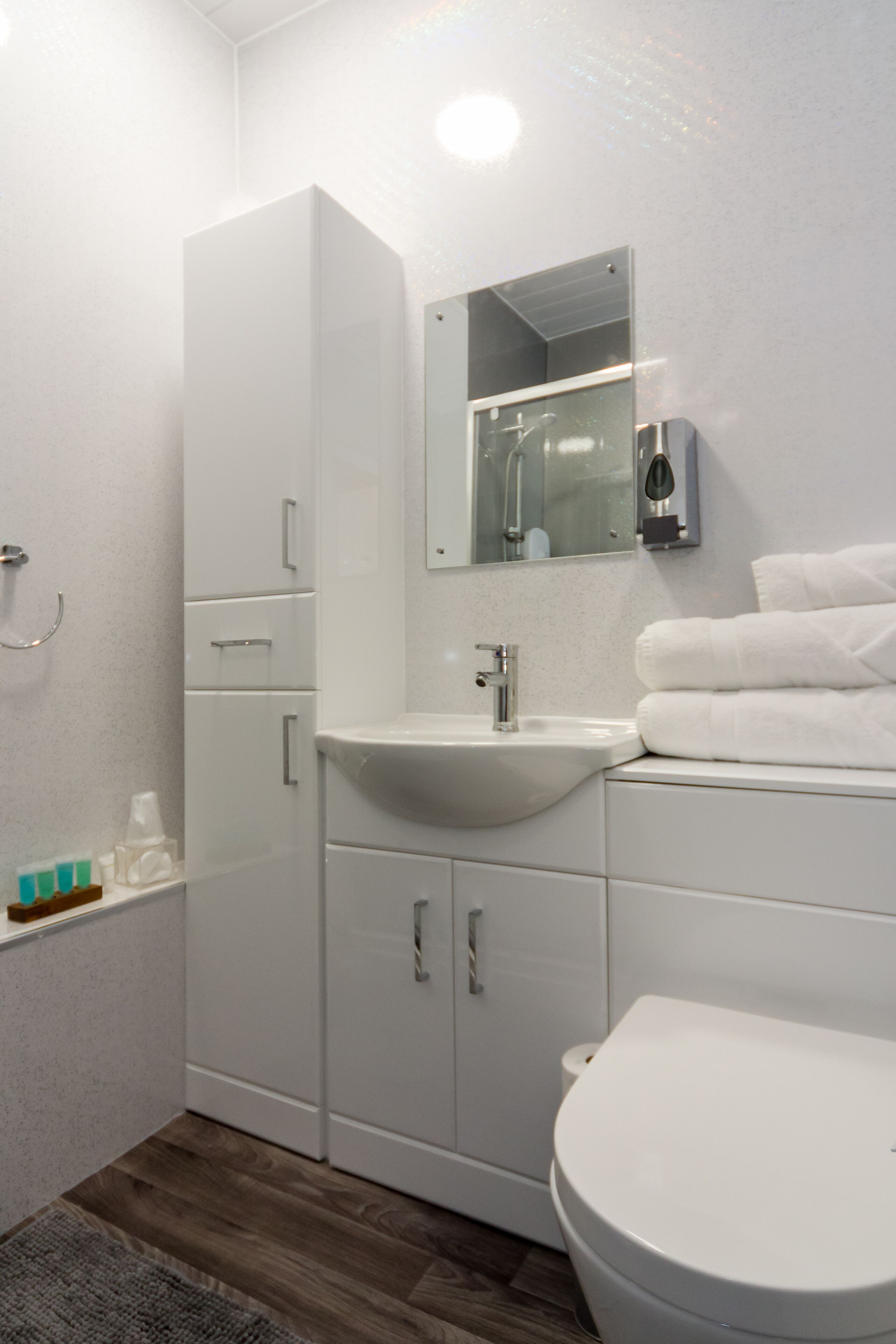 A modern bathroom with a white sink, mirror, and toilet. There are cabinets with silver handles and a towel rack with folded towels.