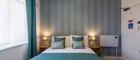 Una cama bien tendida con colcha azul y blanca, dos almohadas a juego y dos lámparas de noche.