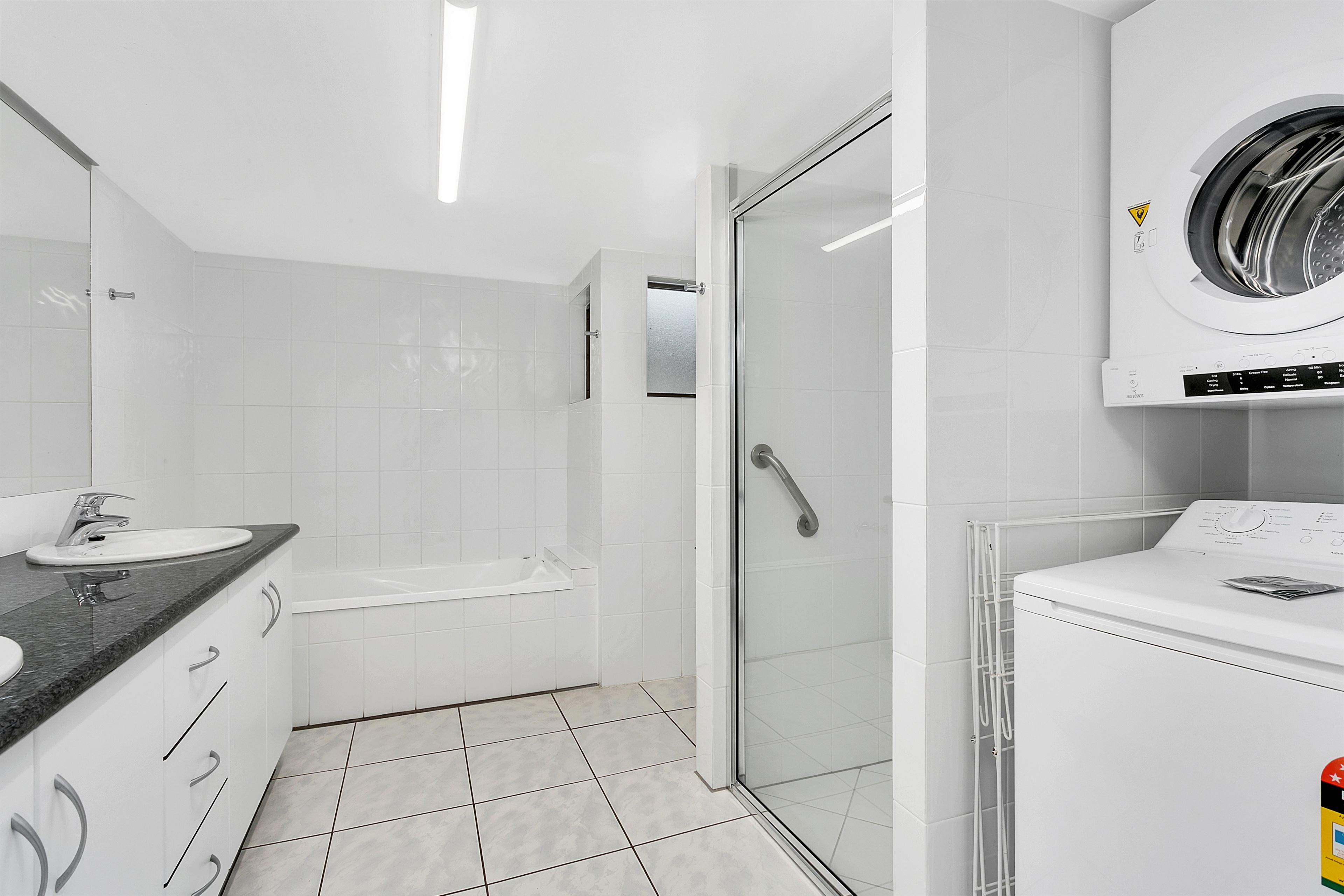 Ein modernes Badezimmer mit Dusche, Toilette, Waschbecken und einer integrierten Waschmaschine.