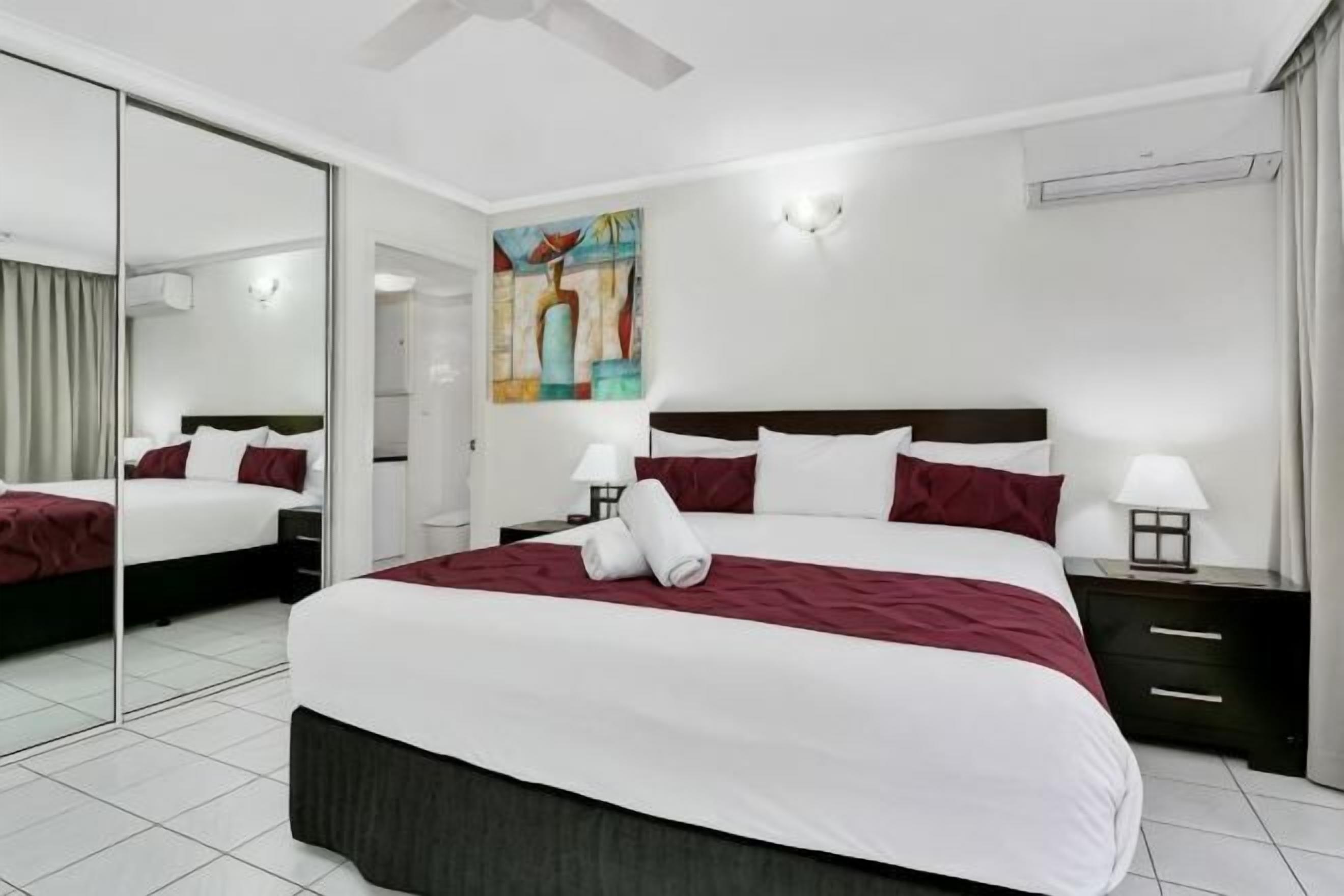 Una habitación de hotel moderna con una cama grande, una mesita de noche con lámpara, un espejo y un cuadro en la pared.