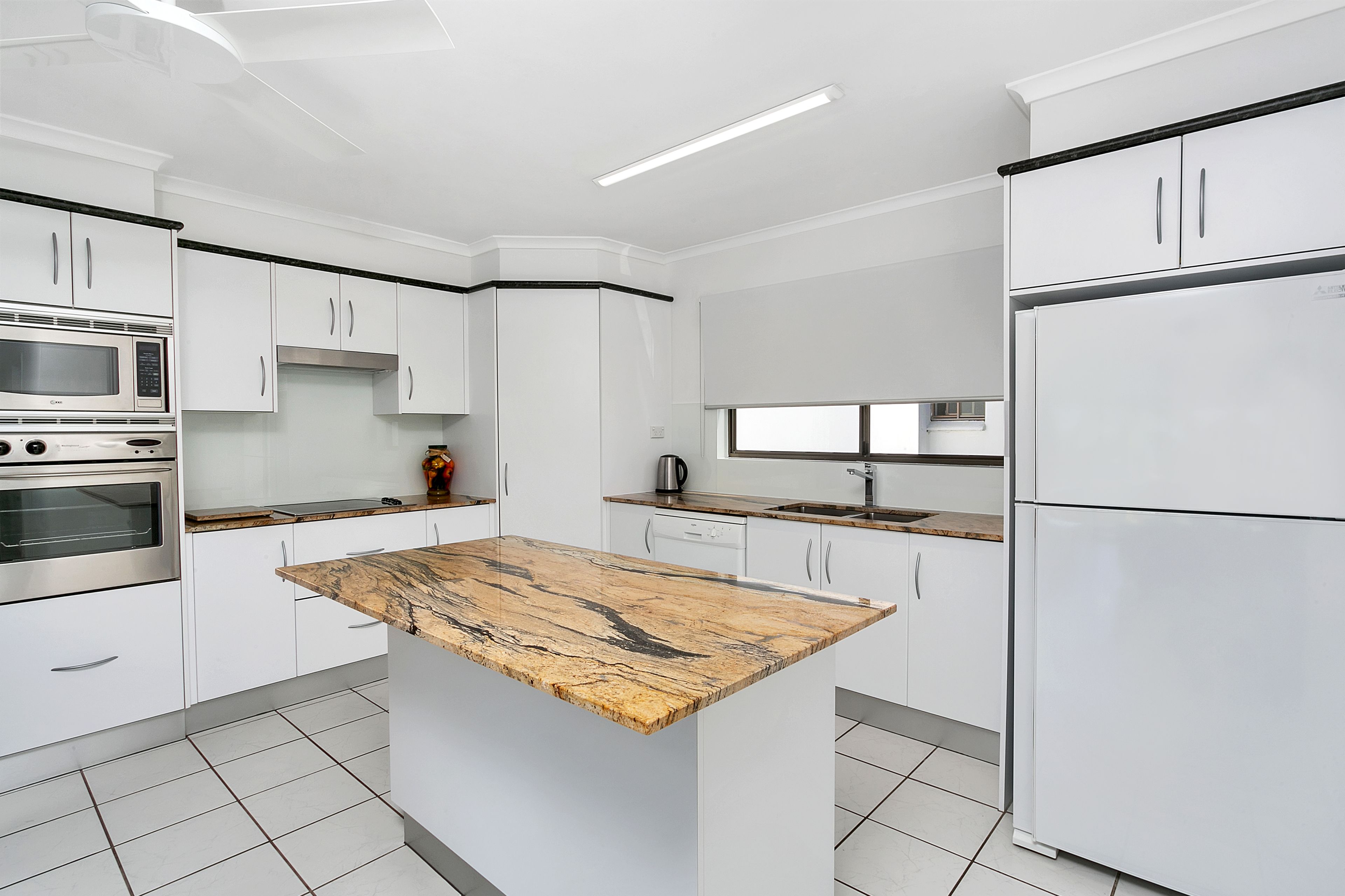 Una cucina moderna con mobili bianchi, un'isola centrale con piano di lavoro in marmo, elettrodomestici in acciaio inossidabile e una finestra sopra il lavello.