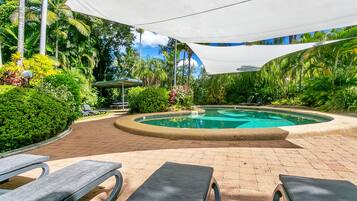 Un espace piscine comprenant des chaises longues, une piscine et une végétation luxuriante tout autour.